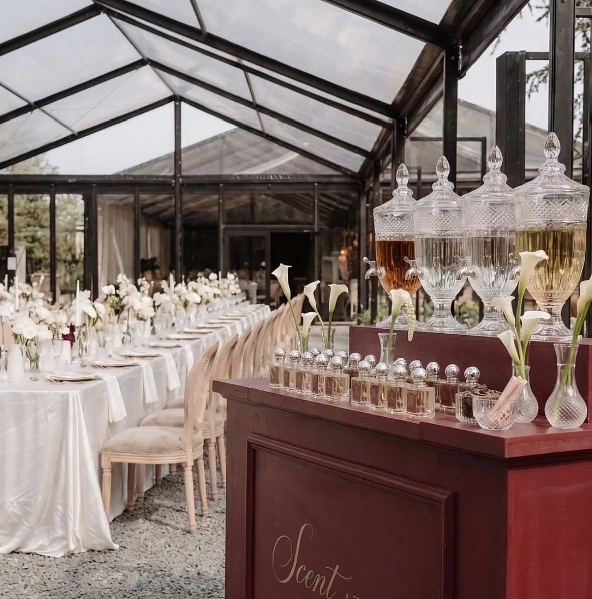Parfemski bar Scent Atelier u staklenom šatoru — kristalni dozatori, niz bočica od 30 ml i kale uz dugački svadbeni stol.
